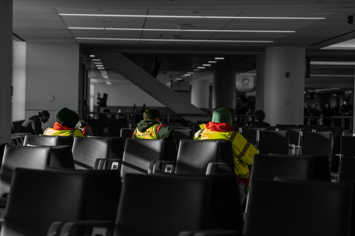 Airport workers in safety vests seated in terminal chairs near an international gate